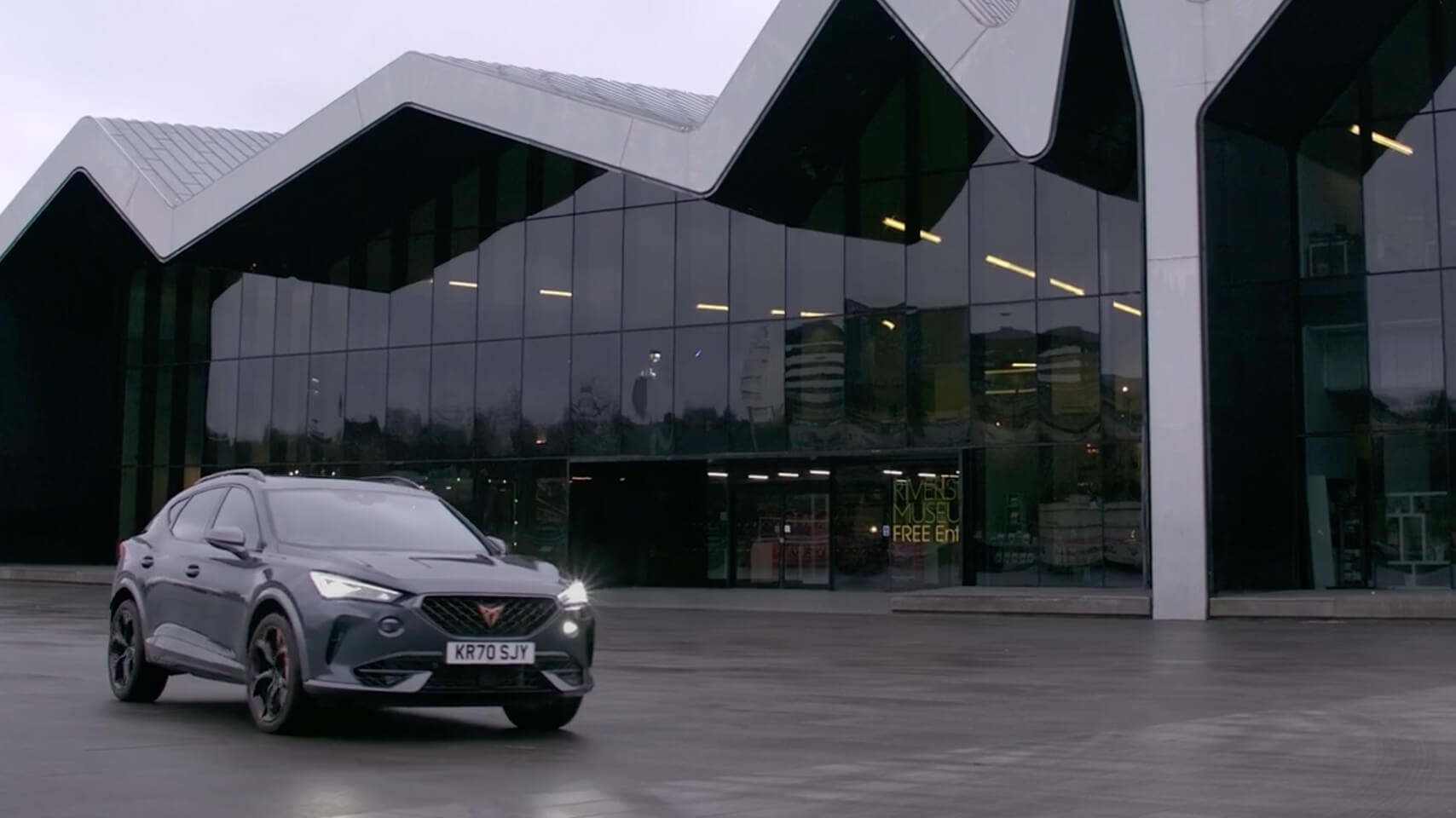 A CUPRA Formentor outside of a building with large windows and slanted roof.