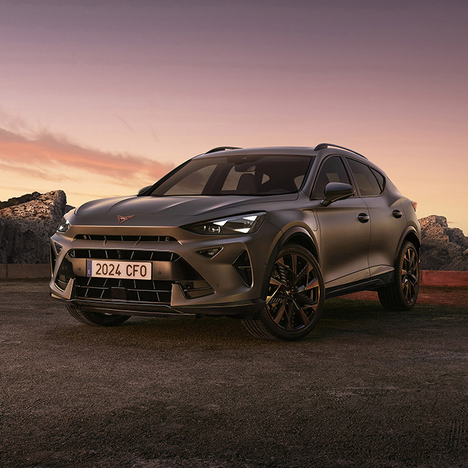 A three-quarter view of the new CUPRA Formentor 2024 parked on gravel at dusk, featuring a sleek, metallic body against a backdrop of rugged cliffs and ethereal sunset.