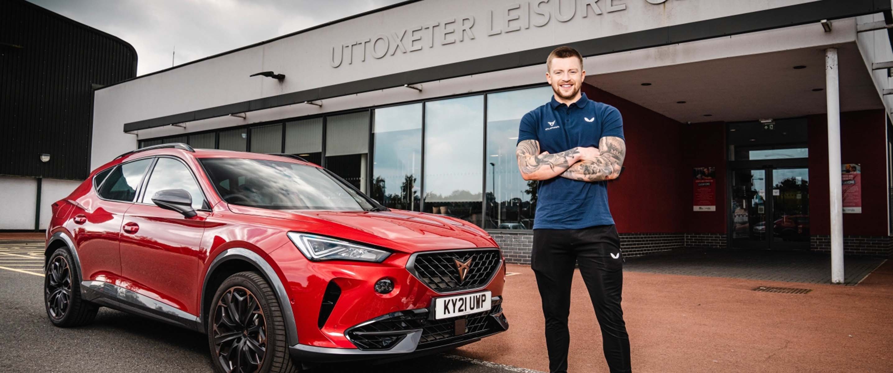 Adam Peaty standing next to a red CUPRA Formentor outside of Uttoxeter Leisure Centre