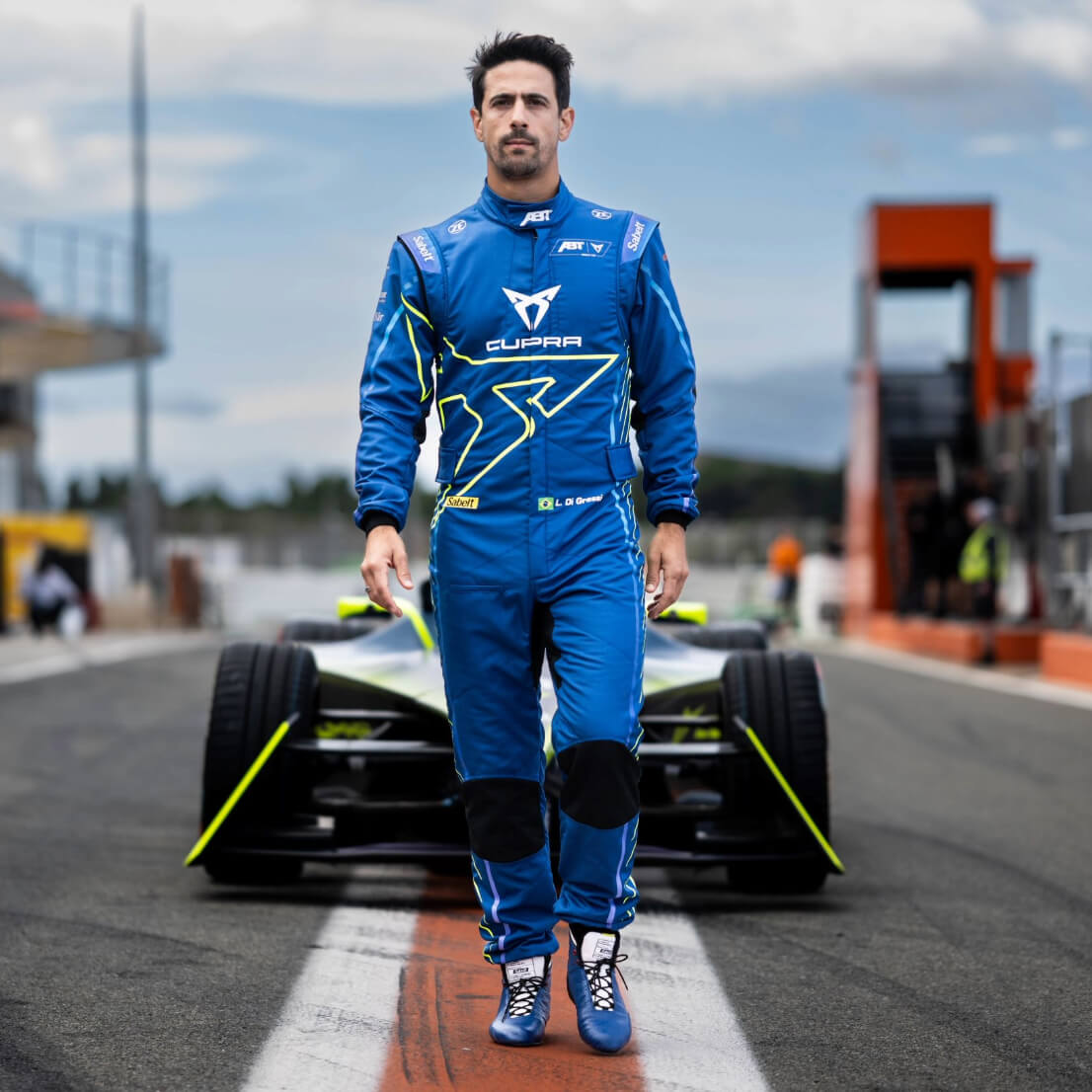 Lucas di Grassi walking on a racetrack in front of a stationary Formula E car
