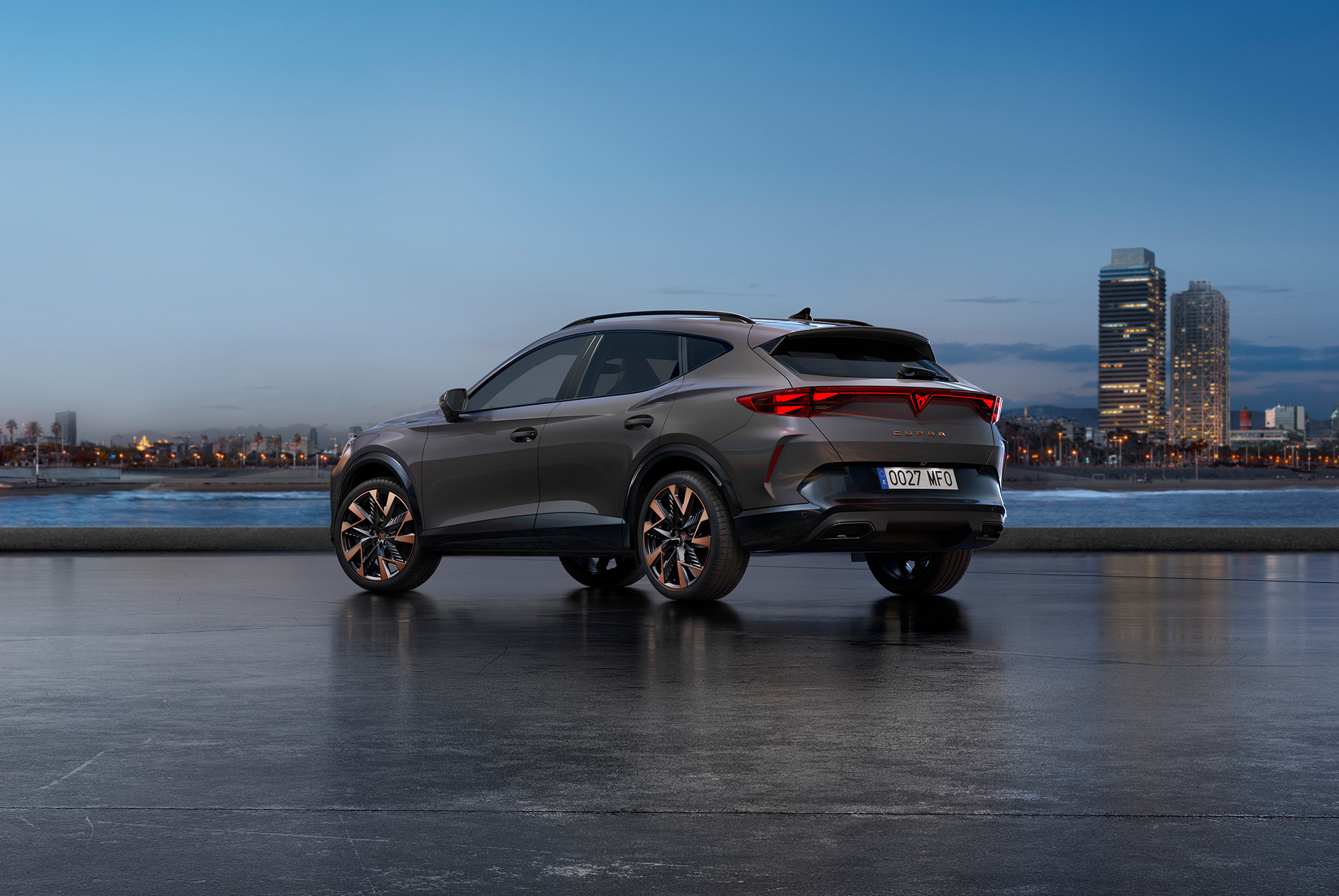 A new cupra formentor 2024 graphene grey CUV parked on a waterfront promenade during twilight. The background features a cityscape with skyscrapers and palm trees illuminated by the fading light of the day.