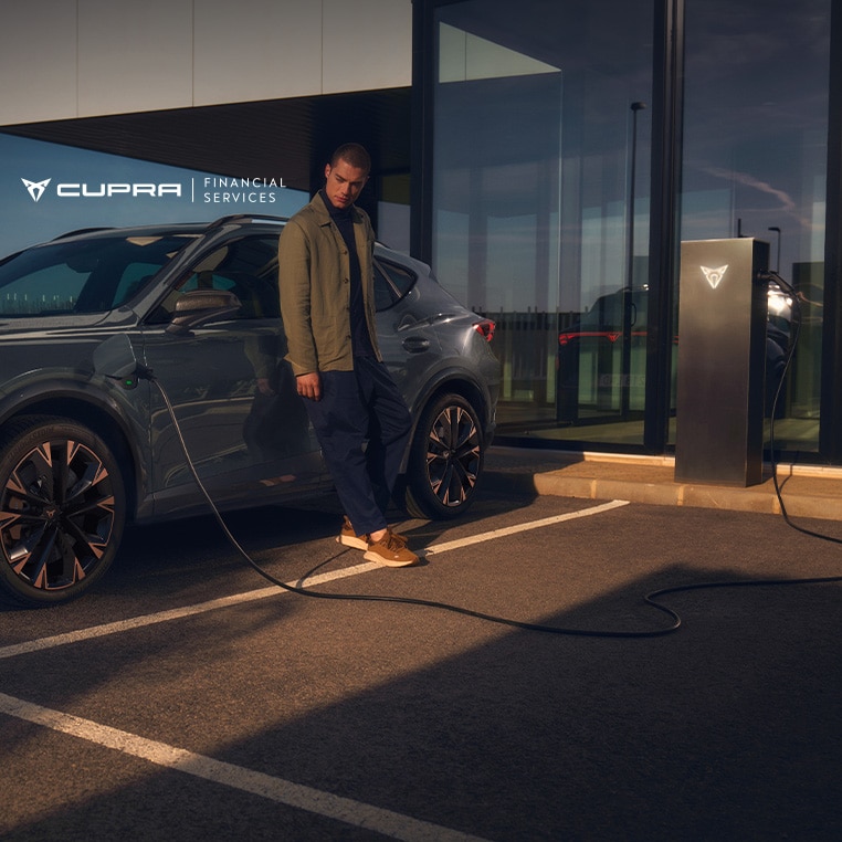 A man leaning on the side of a CUPRA Formentor e-HYBRID that's being charged