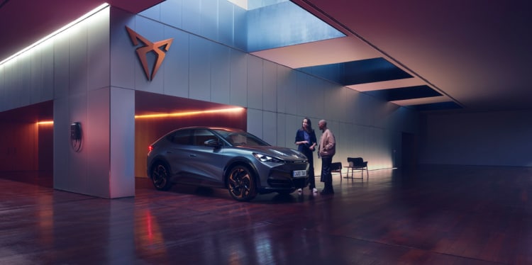 A Tavascan at a CUPRA service centre with a customer and a CUPRA representative standing and talking next to it