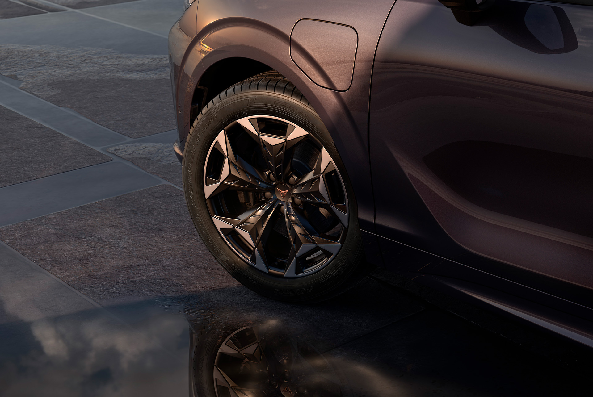 19 inch cosmic alloy wheel on the new cupra terramar, in black with copper accents. Background includes a tiled pavement and part of the car's glossy, dark body.