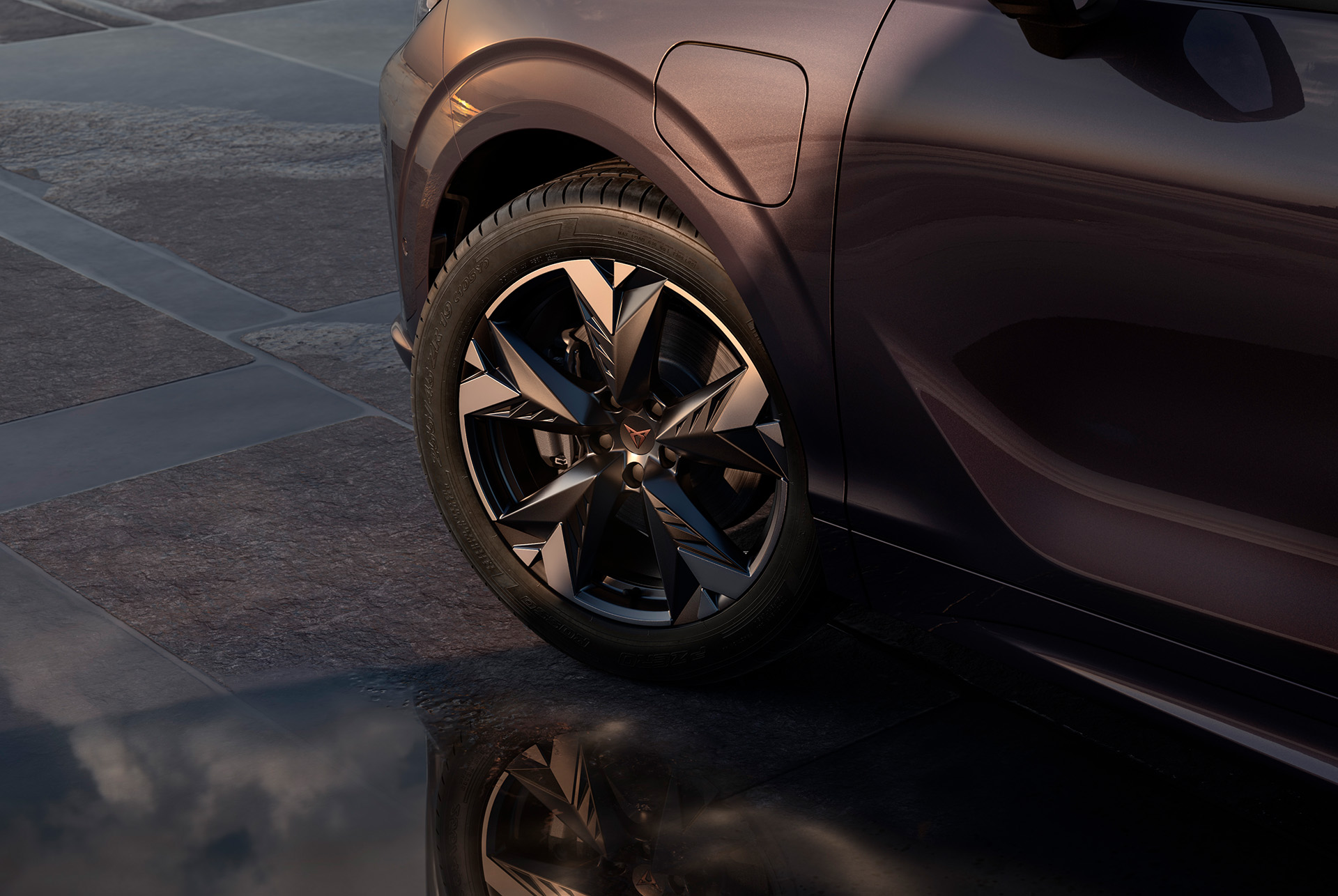 19 inch spectrum alloy wheel on the new cupra terramar, in black with copper accents. Background includes a tiled pavement and part of the car's glossy, dark body.