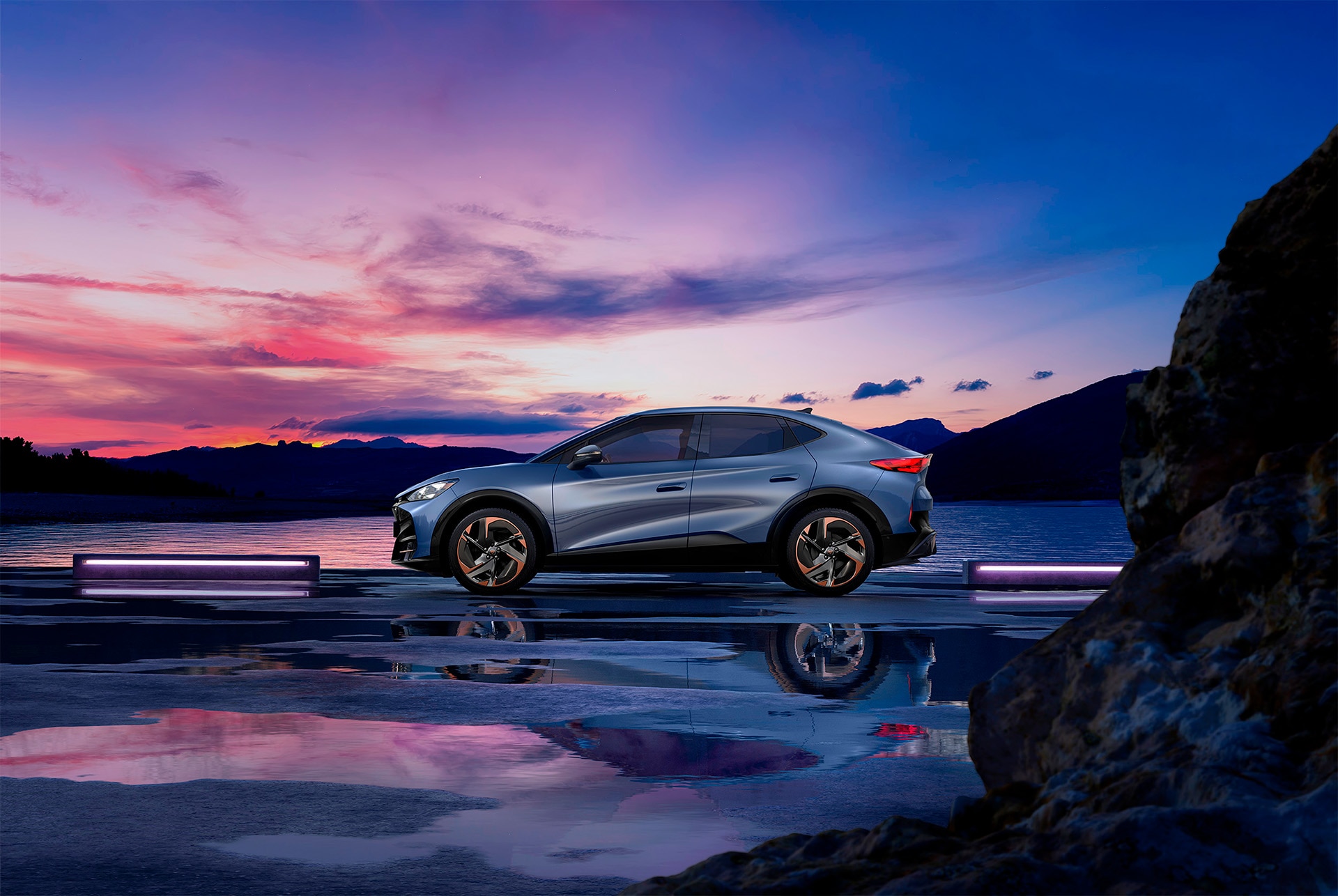 a light blue CUPRA Tavascan parked by a lake with a pink and purple sky in the background