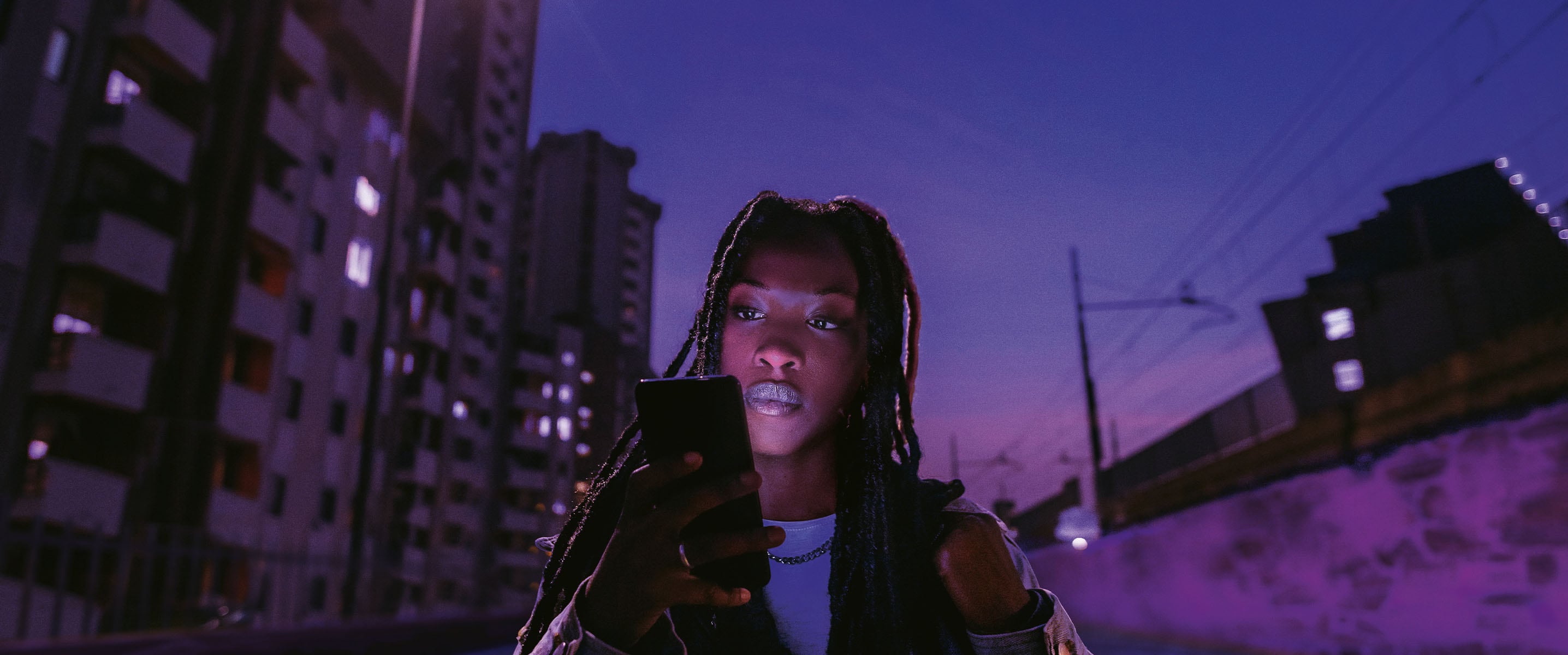 a woman using her mobile phone at night with a dark purple sky behind her